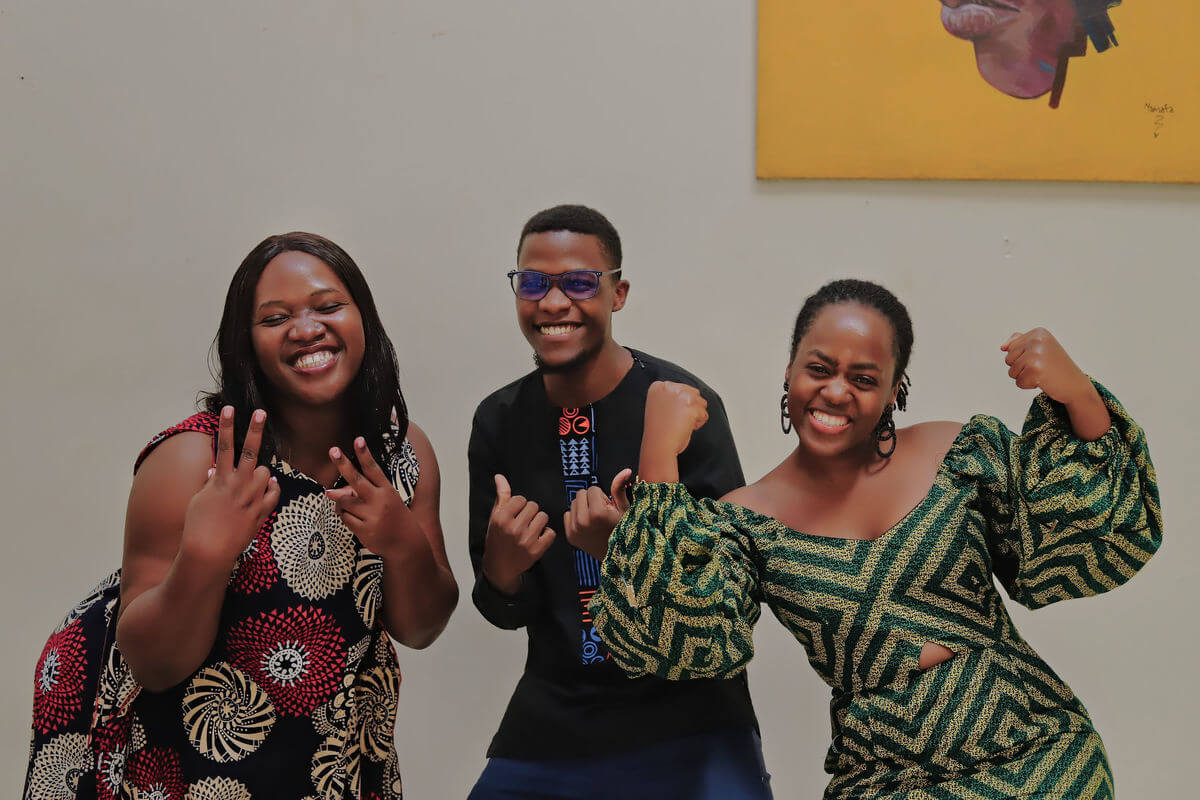 Auf dem Foto sind drei Menschen mit schwarzer Hautfarbe zu sehen - zwei Mädchen und ein Junge. Sie grinsen fröhlich in die Kamera und freuen sich sichtlich.