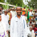 An ophthalmologist standing in front of a crowd of people looking and smiling at the camera.