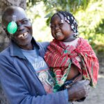 Franciscu from Mozambique has just had cataract surgery. He holds his laughing granddaughter in his arms and looks into the camera.
