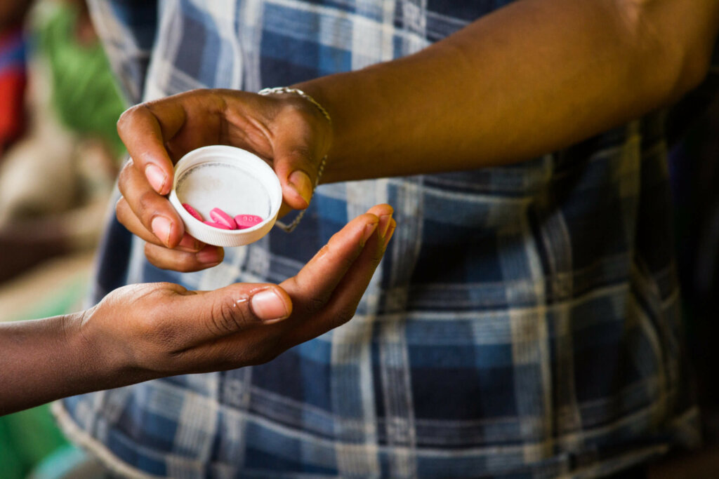 Picture showing hands coming in from each side of the image. The hand on the right side is holding a cap with 4 pink antibiotics and tilting it onto the left hand.