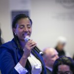 Yetnebersh Nigussie speaks into a microphone at a conference. She is wearing a blue blazer and a white T-shirt.