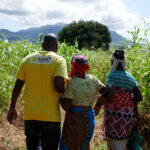 A Light for the World staff member accompanies two women on their way through a field.