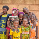 A group of 9 children looking and smiling at the camera. Among them is Neimata who is wearing an eye patch on her right eye.