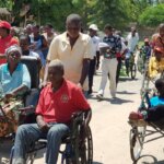 people from the Mozambican disability rights movement including serveral wheelchair users and people with crutches and white canes during a street protest for International Day of Persons with Disabilities.