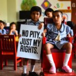 Two children are looking at the camera. One child is holding a sign where 