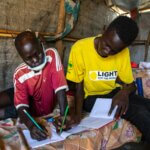 A Light for the World staff member helps young Jima John from South Sudan with his homework. Light for the World cares for people with disabilities in Mahad refugee camp.