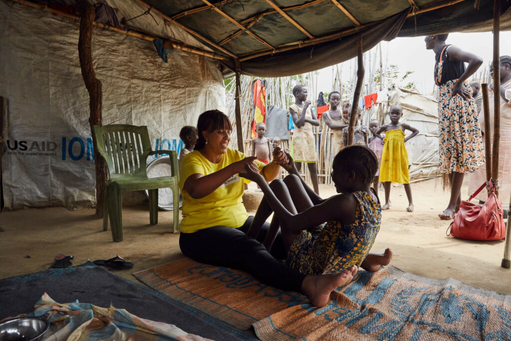 Staff member Sophia Mohammed sits on the ground in the refugee camp in South Sudan helping a girl with her rehabilitation exercises.