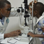 Dr Abel Polaze looks through a device and examines a boy's eyes.