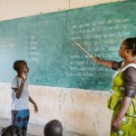 Vincent looks at the blackboard. His teacher points with a stick at a word he seems to be reading.