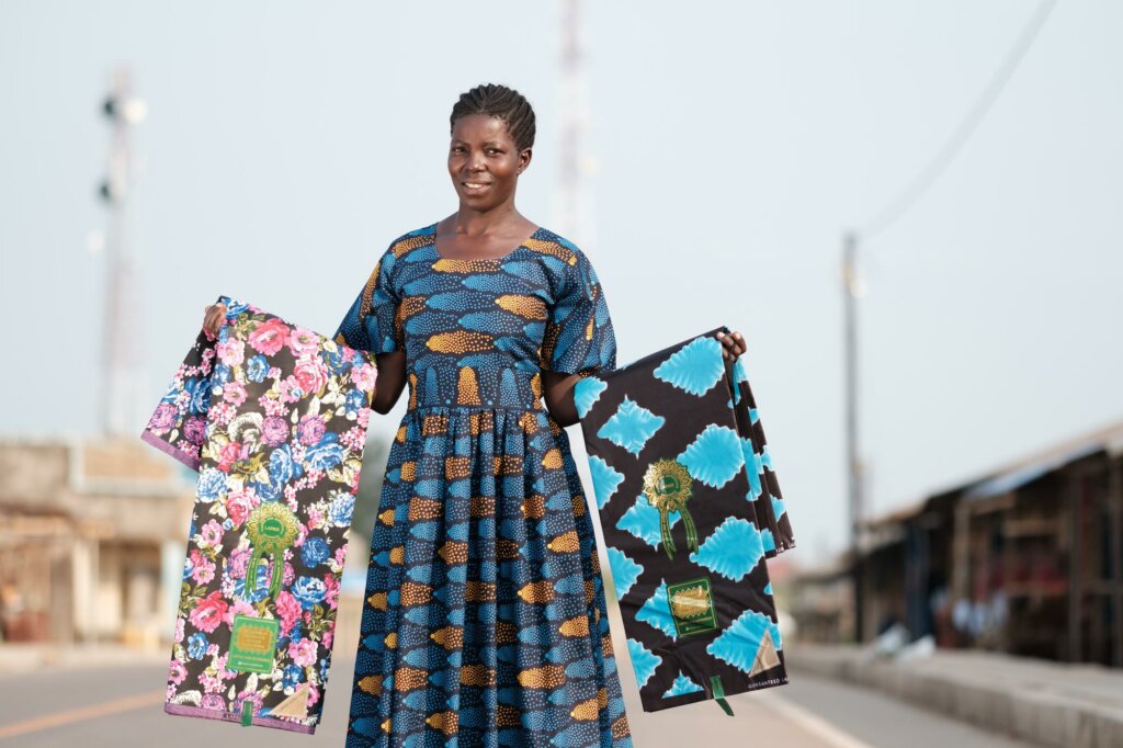 A woman in a blue dress holds two pieces of colourful fabric out wide in her arms