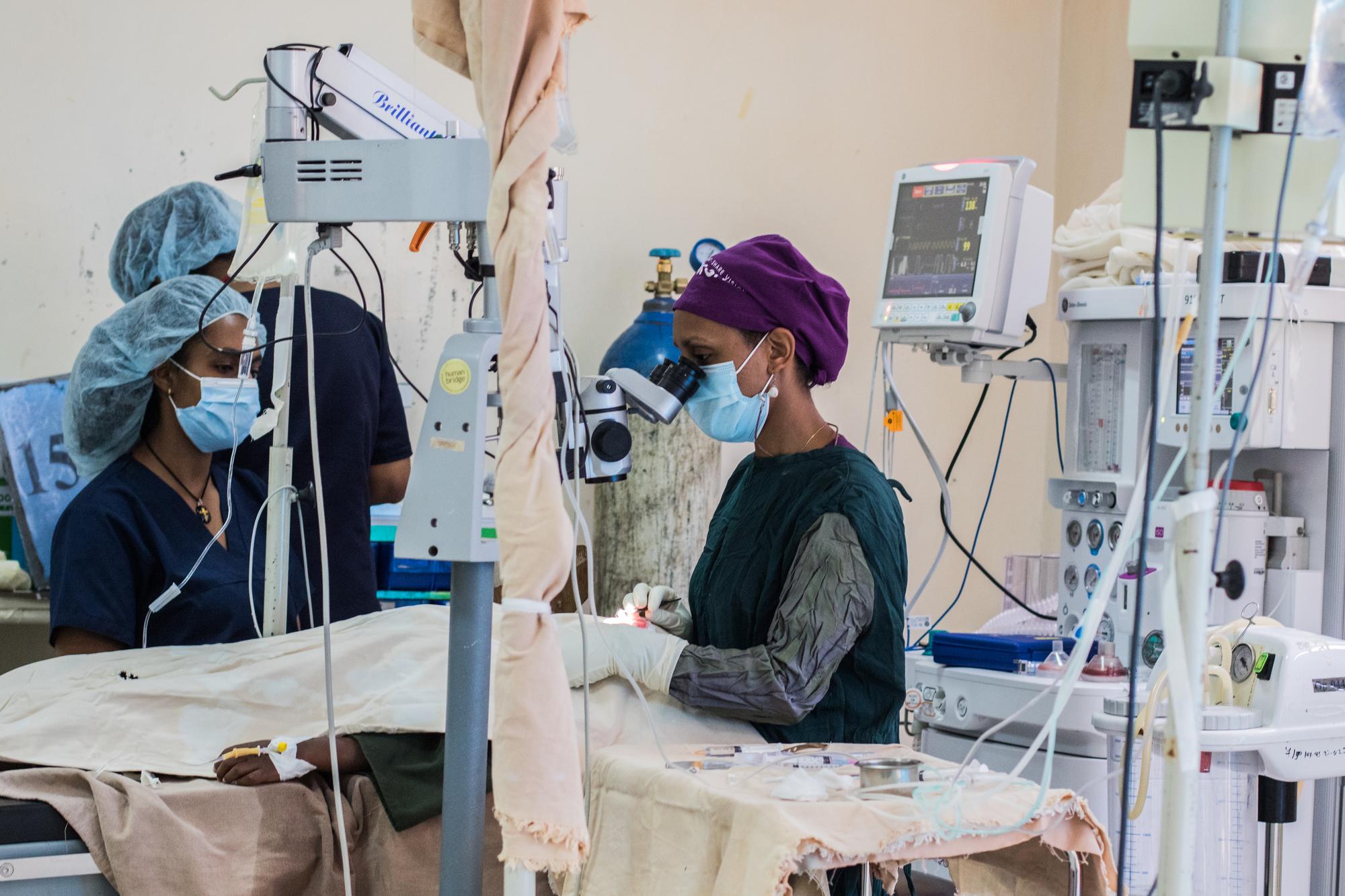 A woman stands in Operation Room and operates on the eyes of the child. The room is full of medical devices and two other nurses who support the operation.