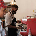 Im Endiro Café wird in Gebärdensprache kommuniziert. Ein junger Mann mit Mundschutz steht vor einer roten Kaffeemaschine und bereitet frischen Kaffee zu.