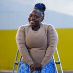 Dorcus Kabahenda is a DIF (Disability Inclusion Facilitator). She is standing upright looking and smiling into the camera. Her crutches are placed underneath her armpits.