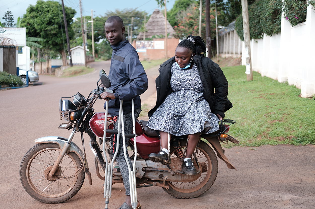 Dorcus on a Ugandan motorcycle taxi called a 'boda boda'. the driver holds her crutches