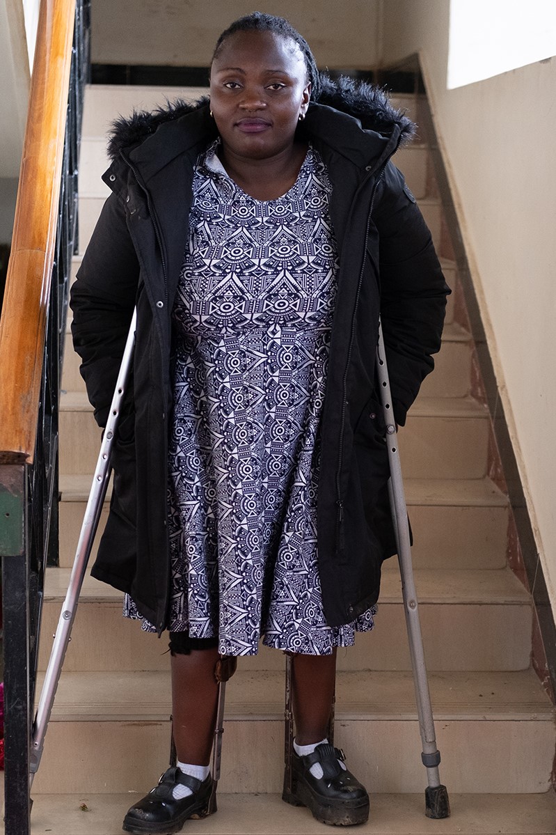 Dorcus stands on a staircase with her crutches. Stairs are difficult to navigate for her, but their is no elevator.