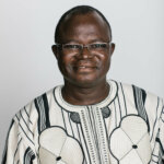 portrait of Elie Bagbila, a middle-aged Burkinabe man with glasses, shortly cropped hair and a traditional white and black cotton shirt.