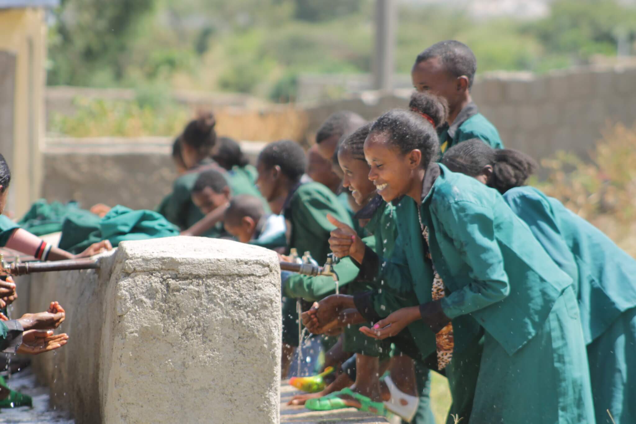 Mädchen aus Äthiopien stehen in grünen Schuluniformen vor Brunnen und waschen sich die Hände.