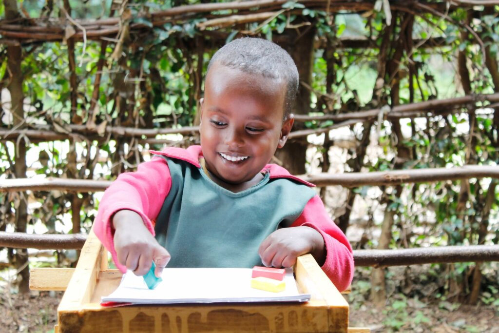 Abdi sits in a lectern with a piece of paper in front of him. He smiles while holding chalk in his hand.