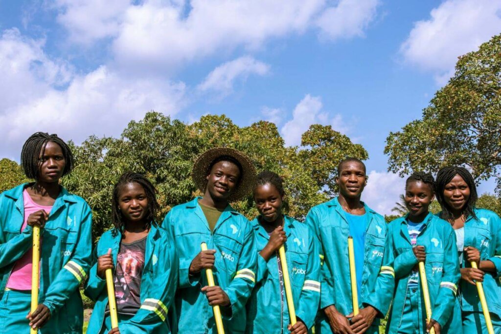 Young Mozambicans in turquois work overalls stand in a group and hold the handles of their work tools.
