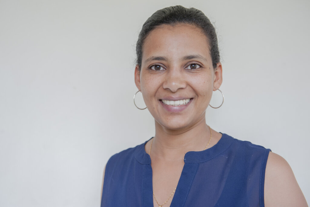 Adugna smiling. The young Ethiopian woman is wearing big silver loop earrings and a blue top