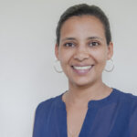 Adugna smiling. The young Ethiopian woman is wearing big silver loop earrings and a blue top