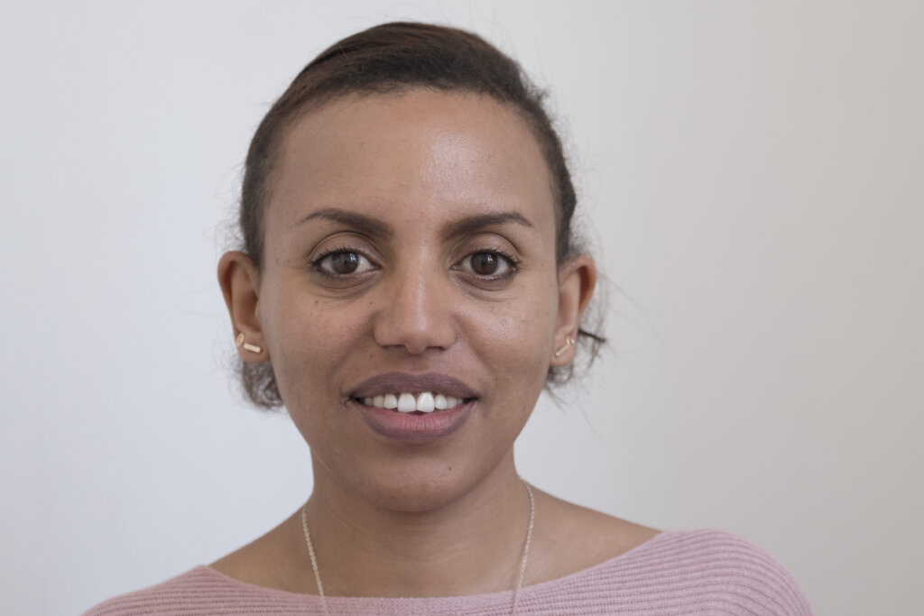 Alem, a young Ethiopian woman in a light pink top looks straight into the camera.