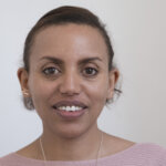 Alem, a young Ethiopian woman in a light pink top looks straight into the camera.