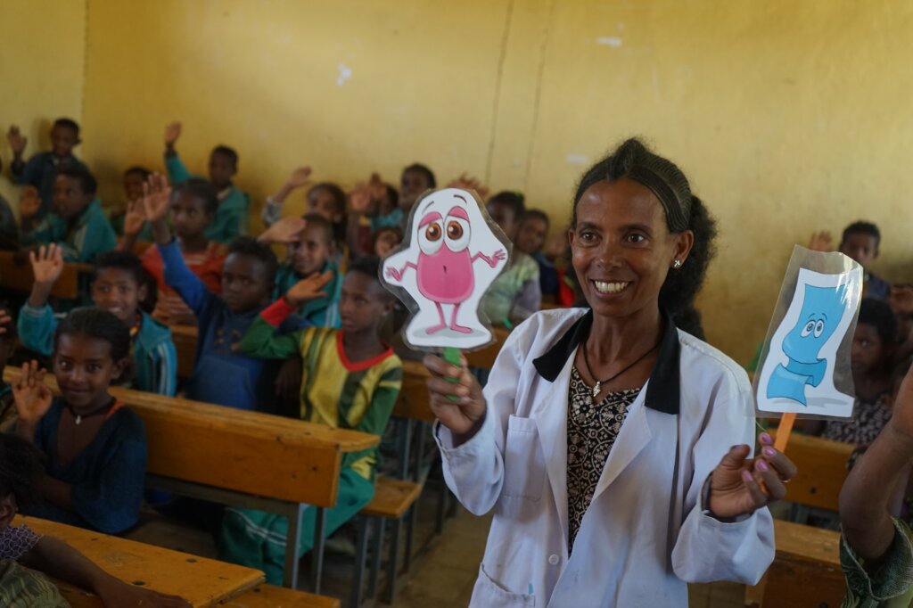 Ethiopian community eye health worker teaching school children about hygiene and trachoma. she holds a cartoon character in her hand.