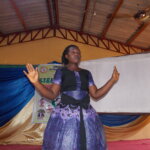 Bernice Adekeye Oyeleke, one of the winners of the Her Abilities Award, is performing a poem she wrote about exclusion. Her arms are spread wide and she is wearing a purple dress.