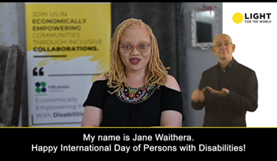 Jane Waithera, Kenyan woman with albinism, speaks on video for International Day of Persons with Disabilities. A white male IS interpreter is to her right.