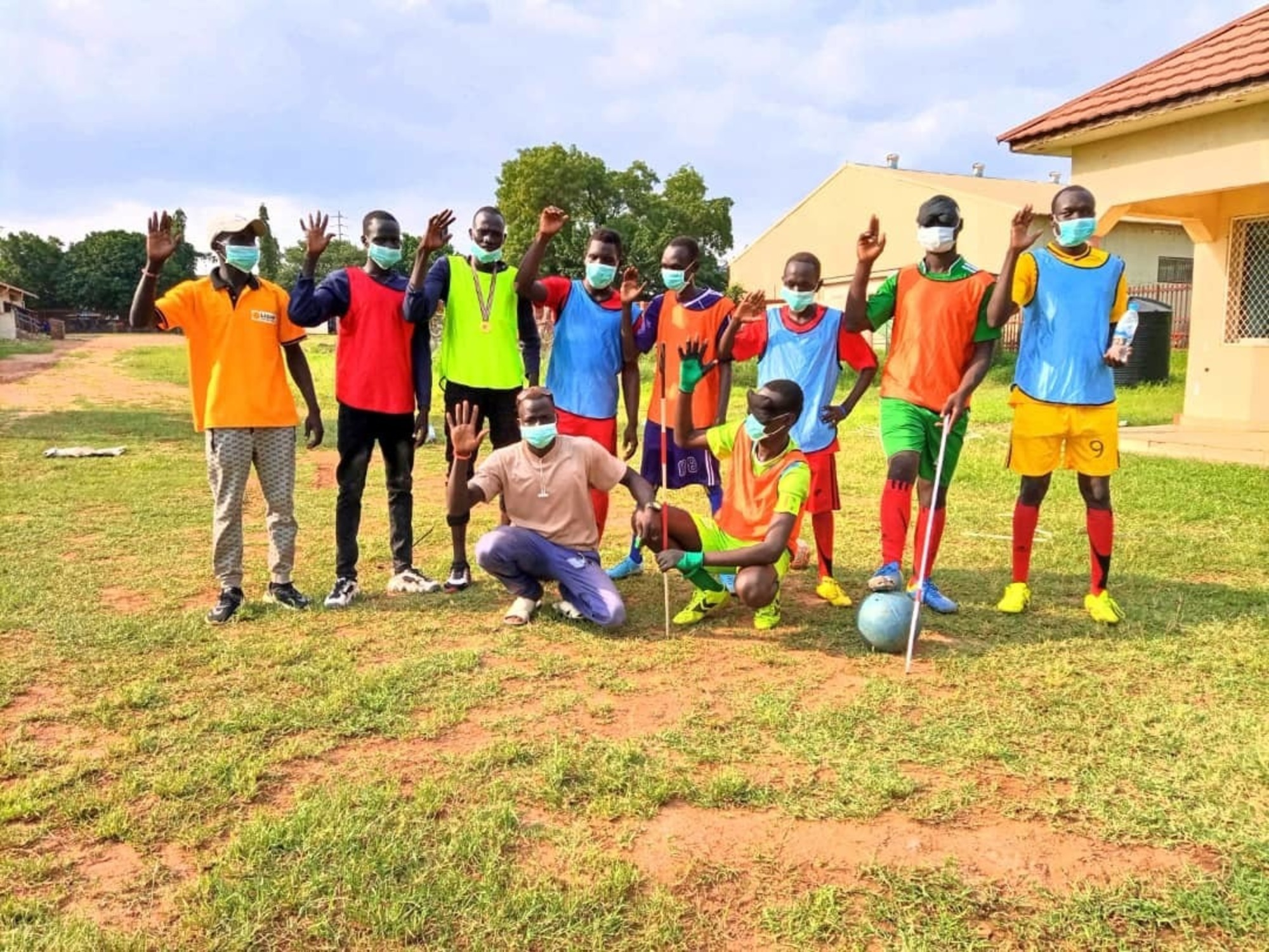 members of South Sudan's first blind football team dressed in their jerseys stand together raising their right hand to show their support for an education campaign.