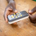 a gray and white EVO10 audio player held in the hands of a Burkinabe student