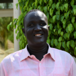 Abilo Theophilos, a South Sudanese blind man with dark skin in a pale pink button-down