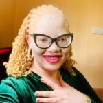 Jane Waithera, Disability Inclusion Adviser at Light for the World Kenya. Jane is a Kenyan woman with albinism. She wears black-rimmed glasses, pink lipstick and shoulder-length blond hair