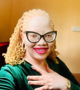 Jane Waithera, Disability Inclusion Adviser at Light for the World Kenya. Jane is a Kenyan woman with albinism. She wears black-rimmed glasses, pink lipstick and shoulder-length blond hair