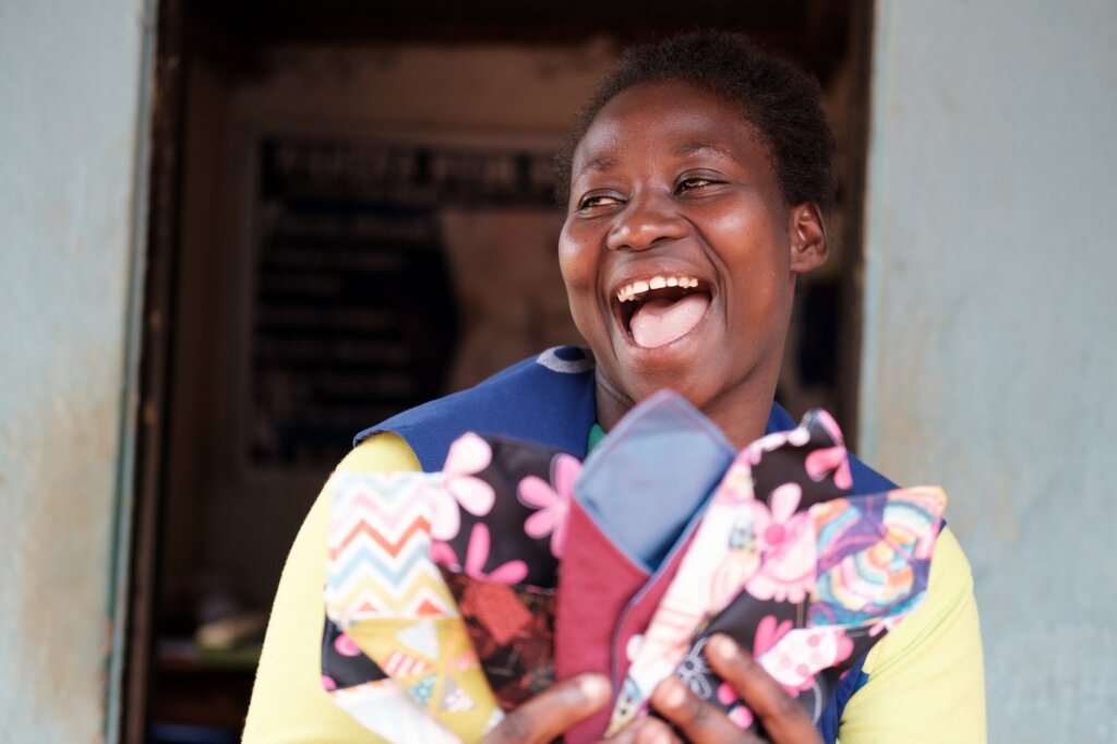 Young Ugandan woman laughing and showing her products - reusable menstruation pads