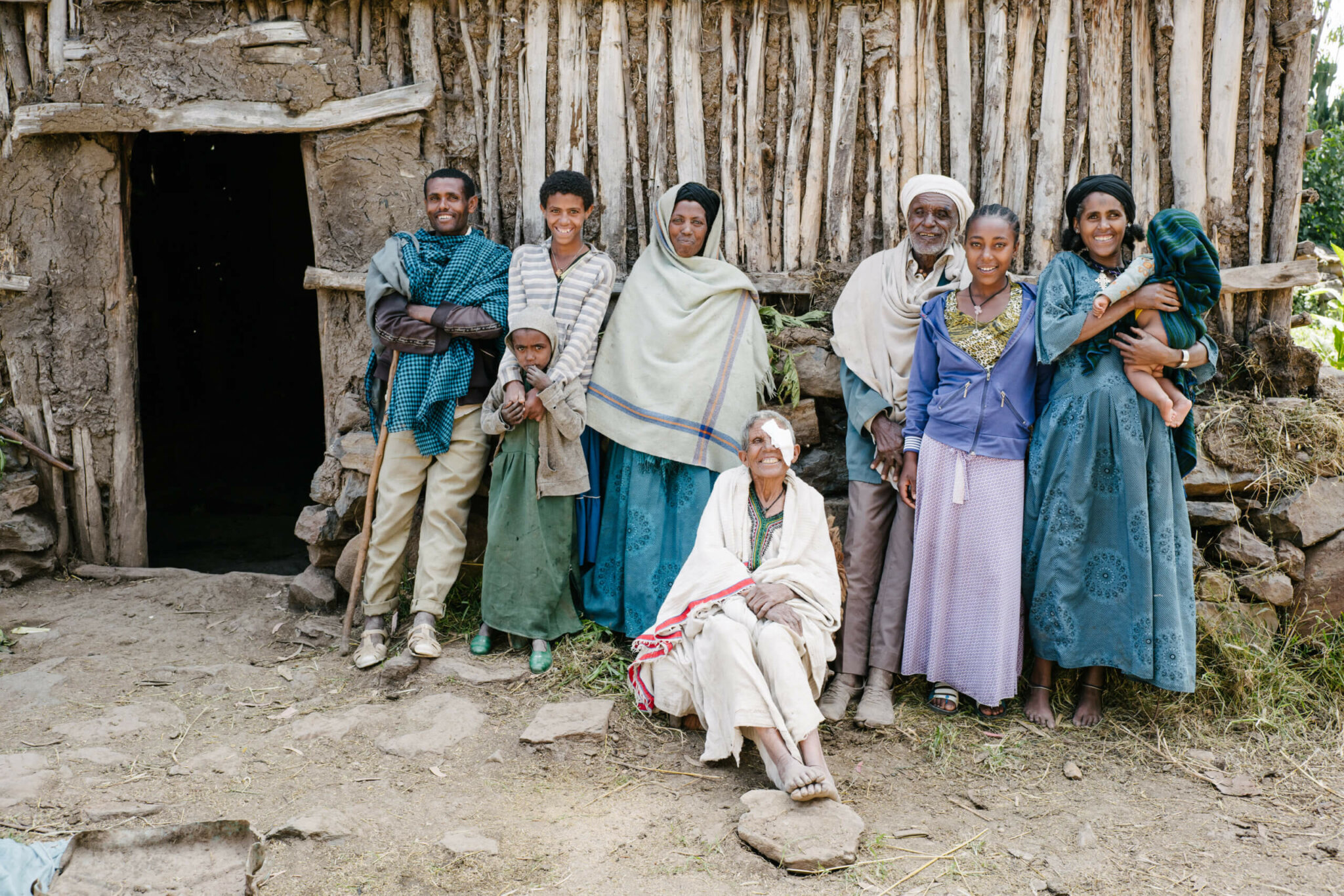 A 60-year old Ethiopian woman in traditional white cotton clothing sits in front of her home surrounded by family members.Dorf und lächelt in die Kamera. Sie ist umringt von ihren Familienmitgliedern, die alle freudig in die Kamera lächeln.