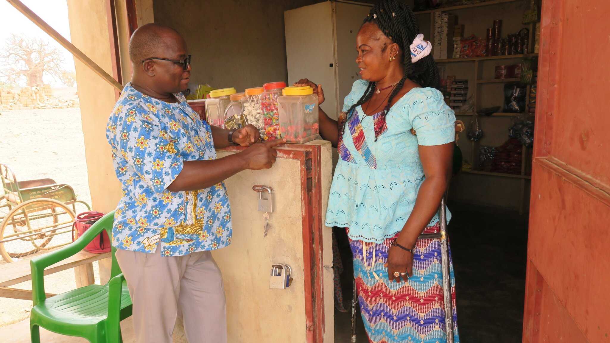 a Burkinabe man and woman talk in front of her marketstall.