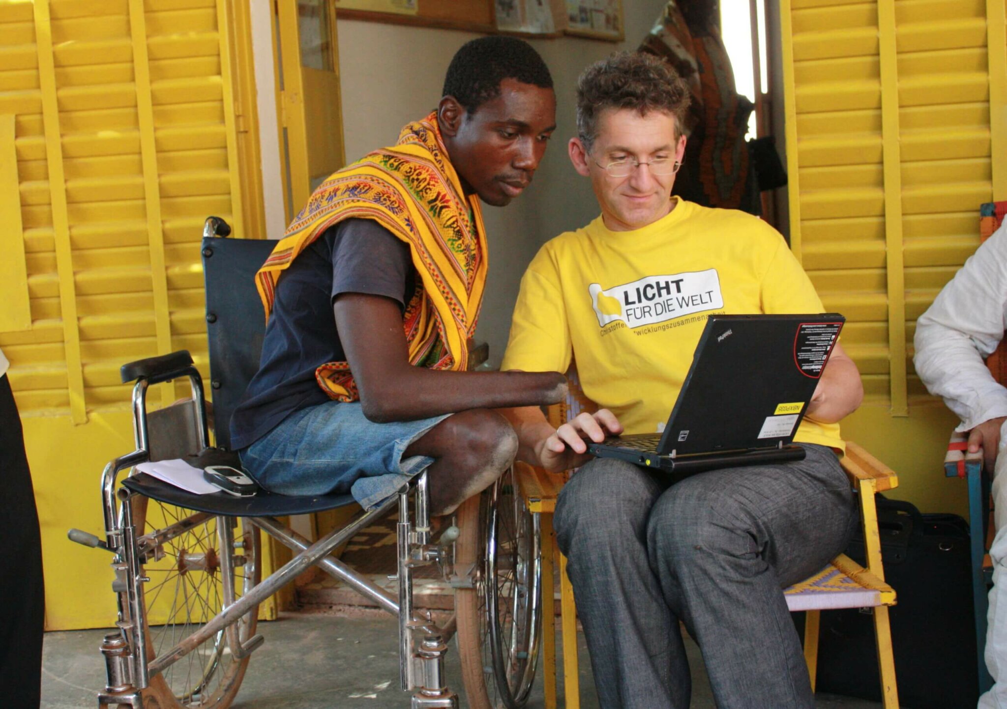 Rupert and a young man in a wheelchair look at his laptop together.
