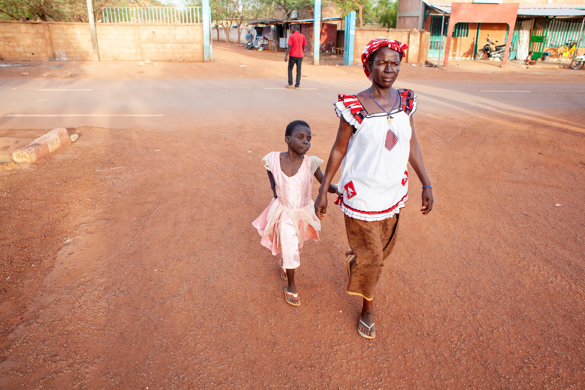 A little girl, Amandine, walks to school with her host mother Therese.