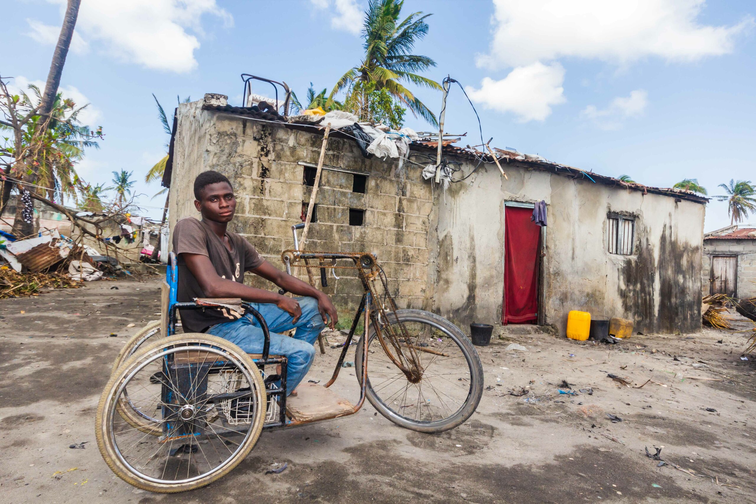 A young man sits in a wheelchair beside his house which has been damaged by high winds