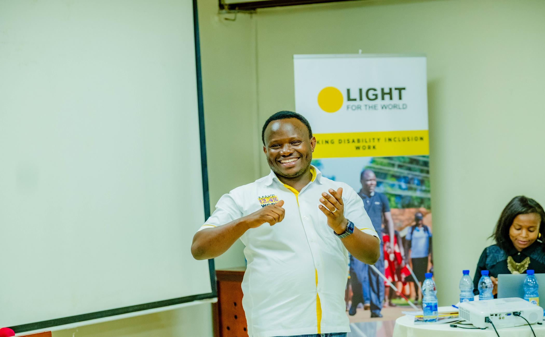 Ambrose Murangira stands smiling in front of a Light for the World sign