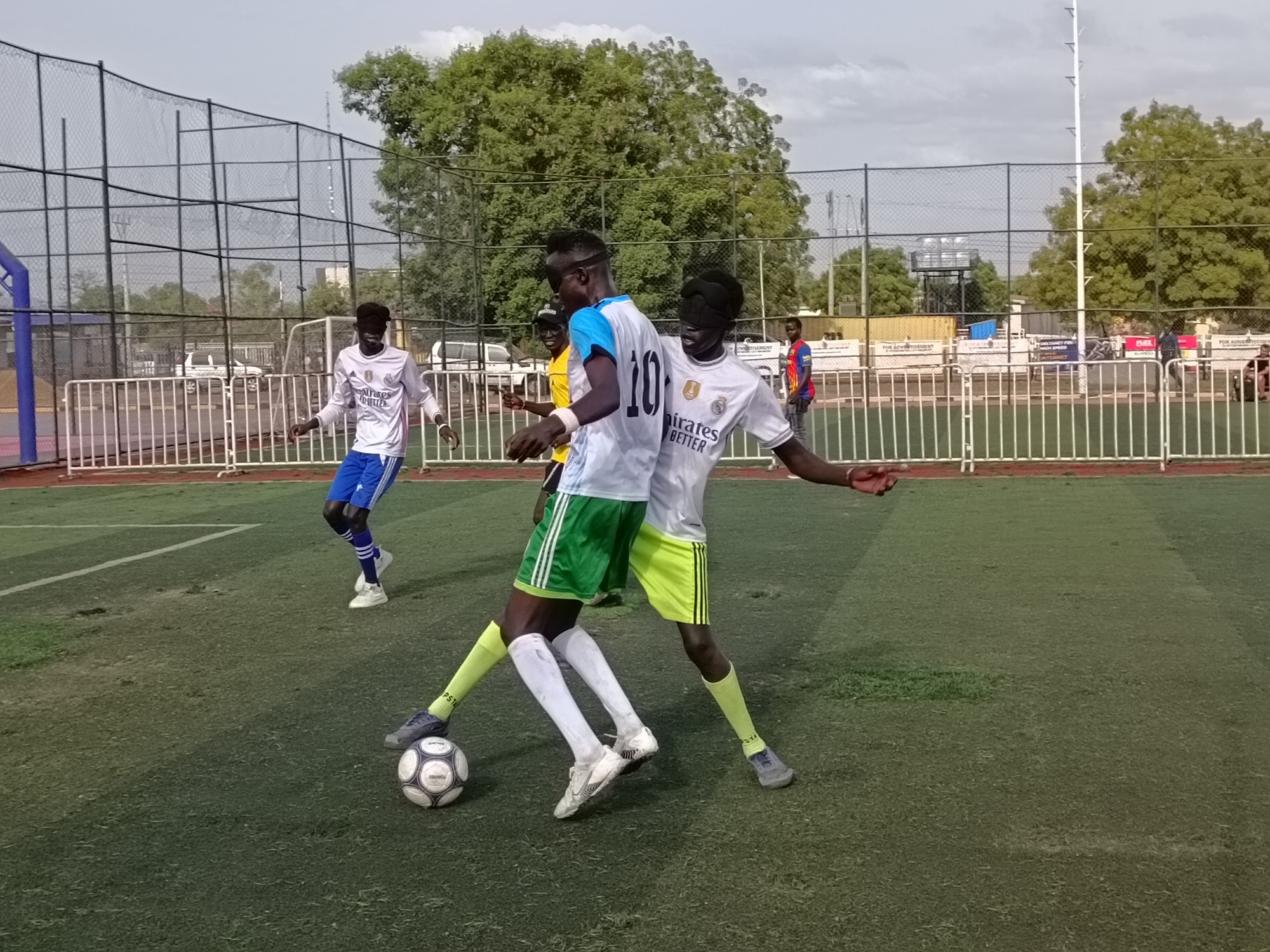 Two football players from the Blind Football team reach for the ball with their foot, as they play on a field in South Sudan.