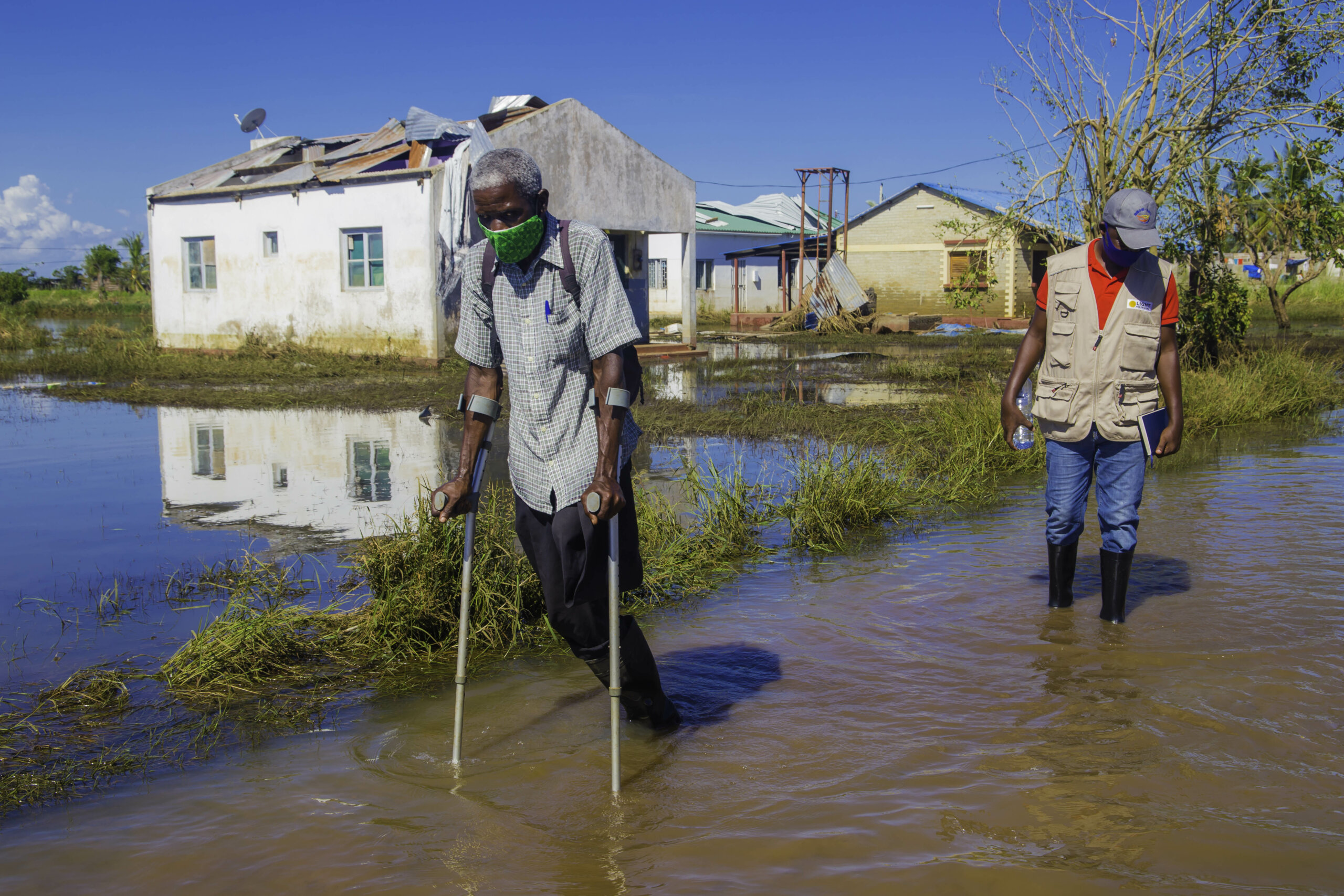 An elderly man with crutches struggles to walk through floods