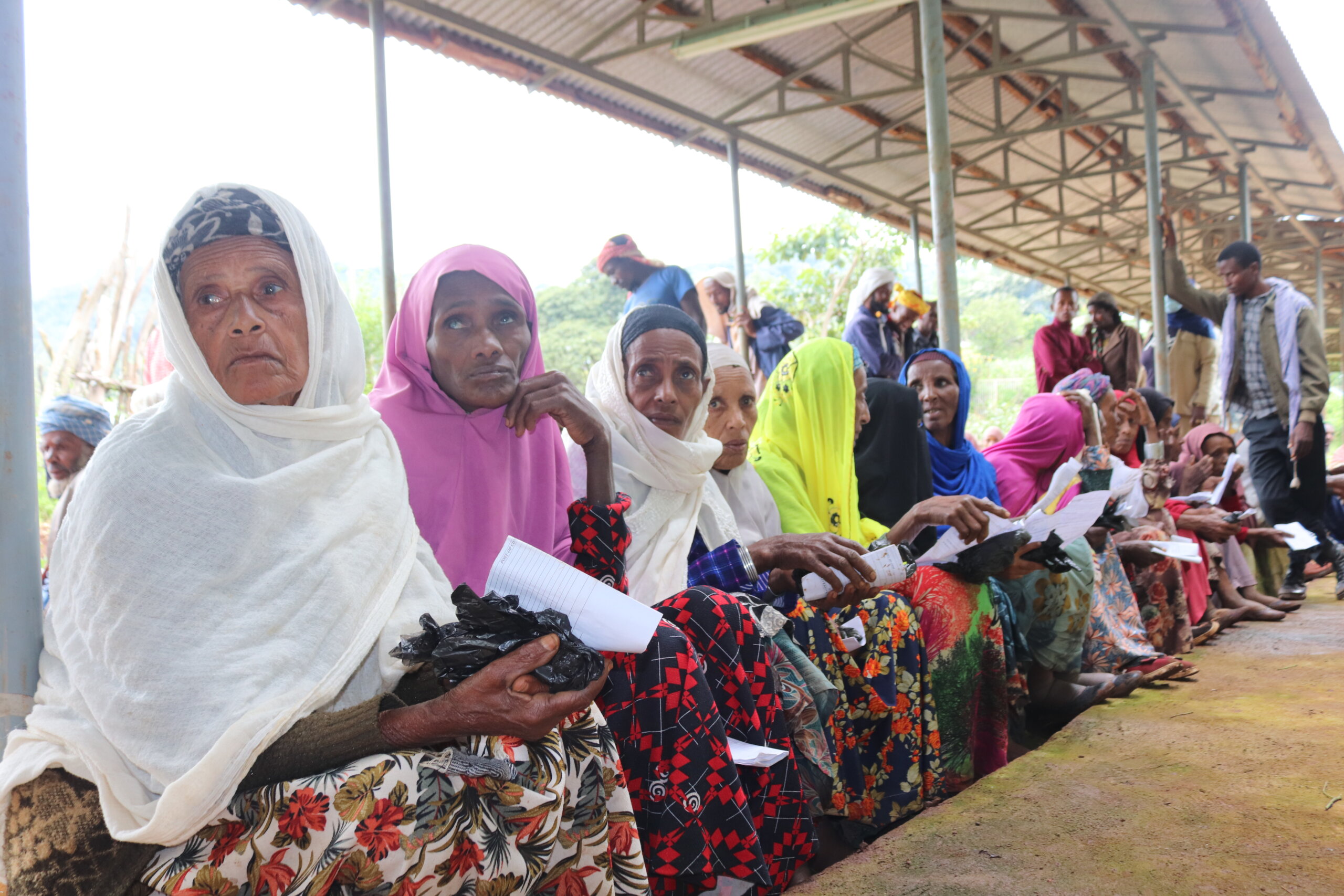 Women in brightly coloured shawls and skirts sit in a queue for eye care in an outdoor waiting area in Ethiopia.