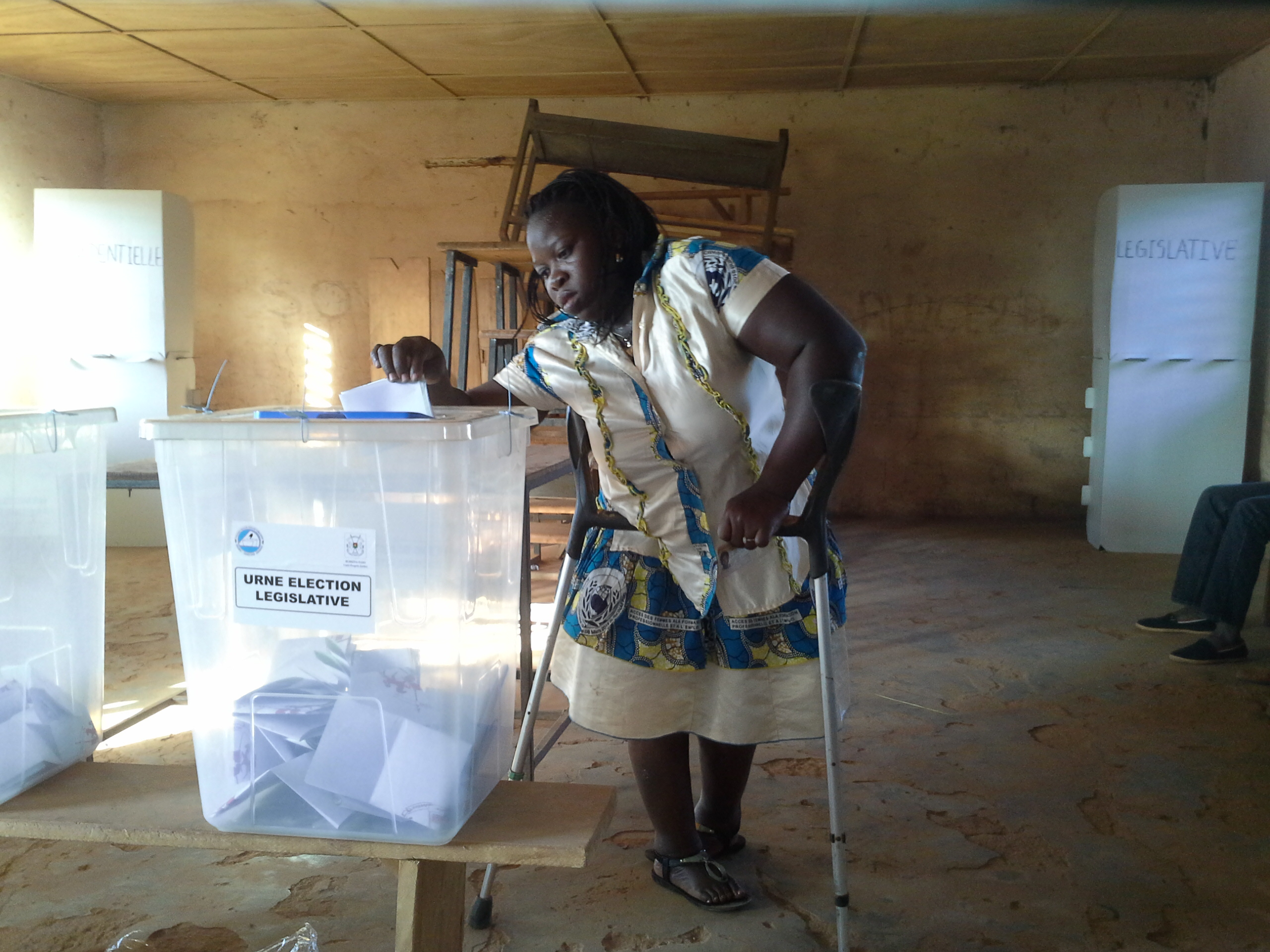 A woman with a disability grasps her walker as she casts her vote during an election in Burkina Faso