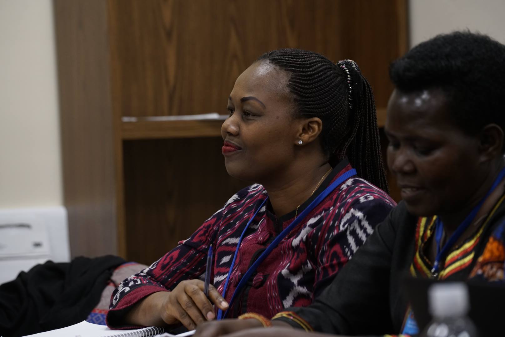 Mathilde, a Rwandan woman with long dreadlocks and wearing a patterned shirt, speaks at a panel table.