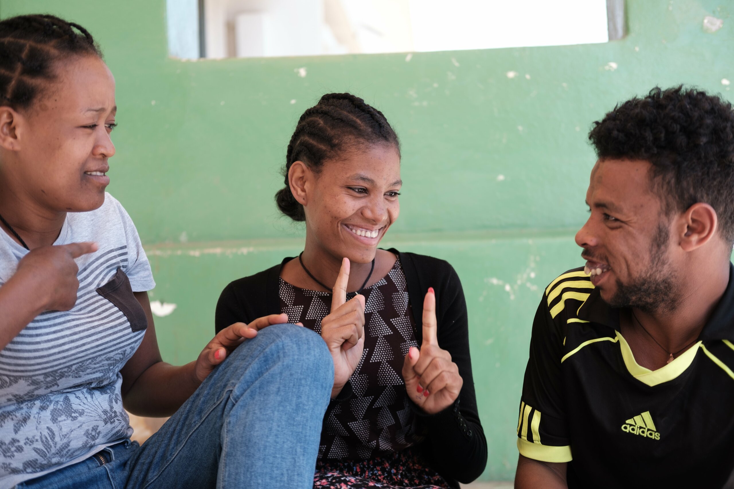 The image shows Mimi (centre) speaking sign language with her two friends on either side of her.
