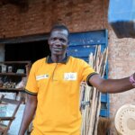Image of Peter Rosario, a Disability Inclusion Facilitator and entrepreneur in Wau, South Sudan. Peter is standing outside his store which sells cigarettes, tea leaves, charcoal, sweets, batteries, cooking oil, blankets and mosquito nets.