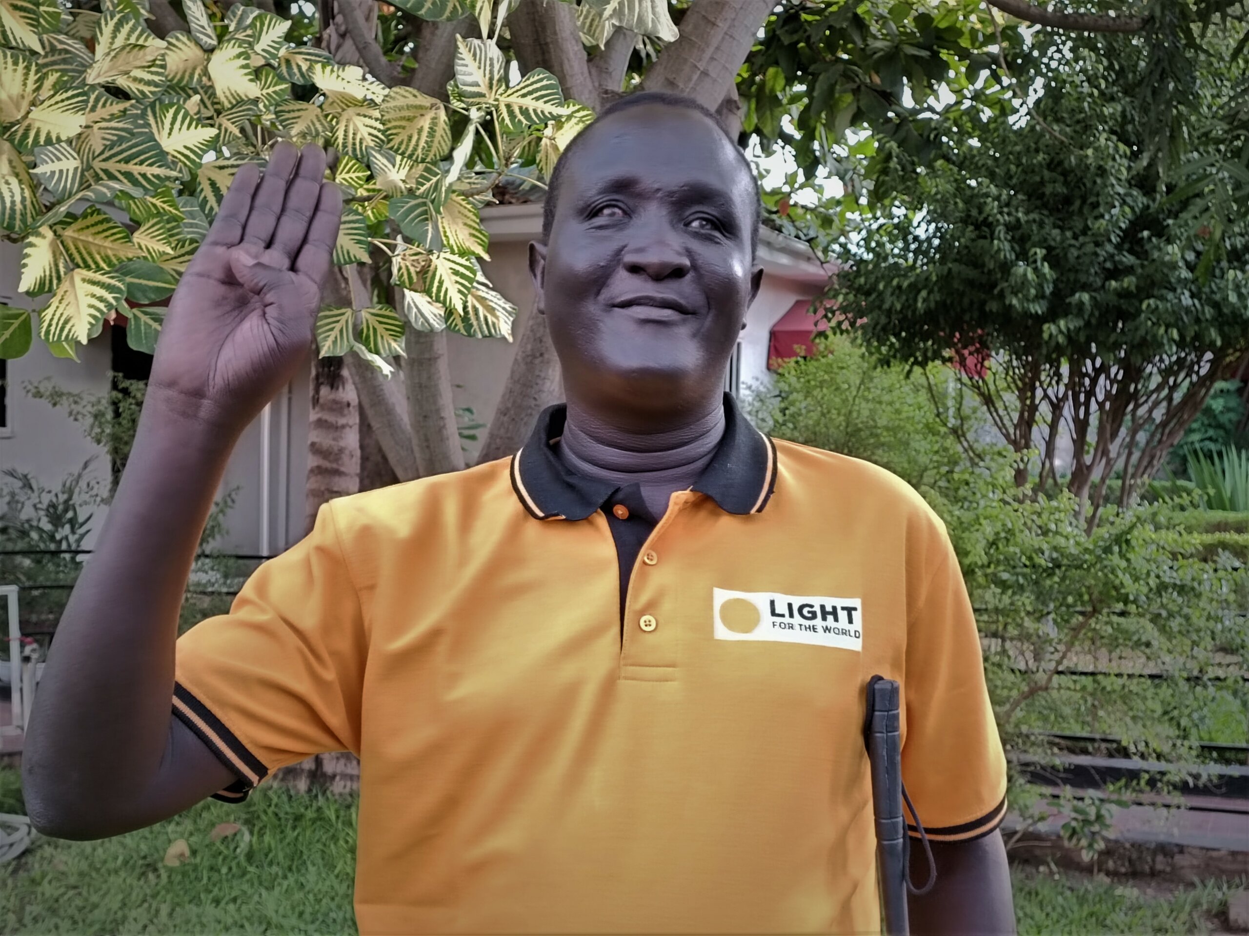 Abilo Theophilus is standing outside smiling, wearing a Light for the World tshirt.